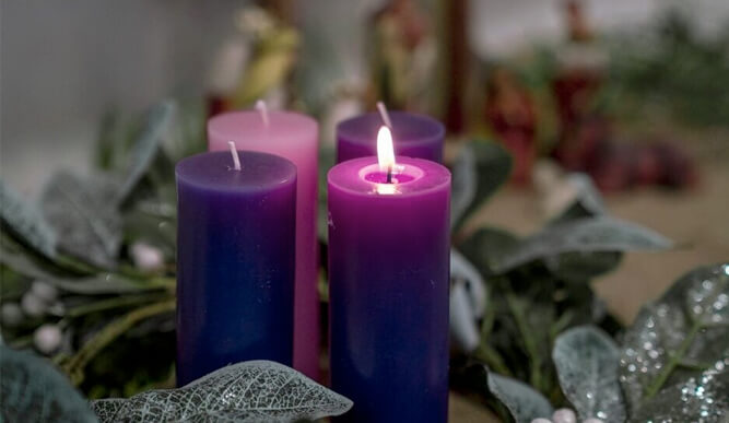 A wooden cross hanging on a purple colored wall.